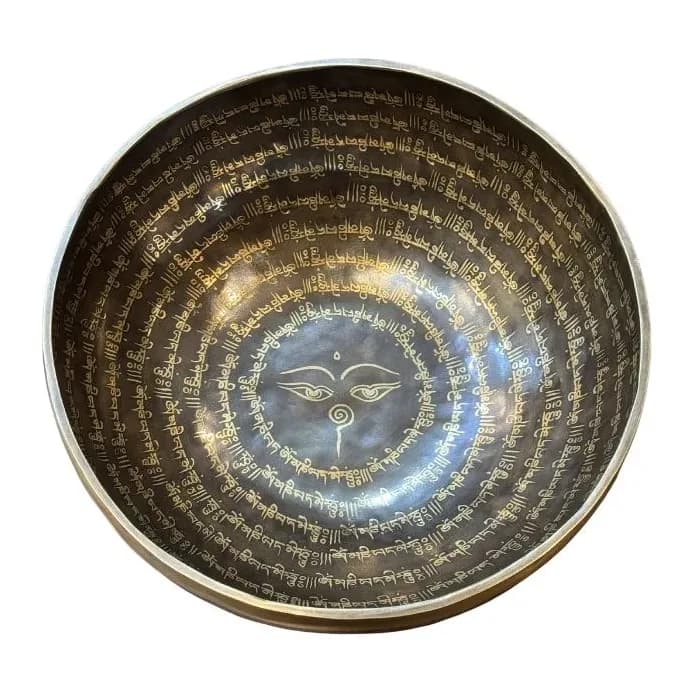 A hand-hammered bronze singing bowl densely etched with mantra script, viewed from above