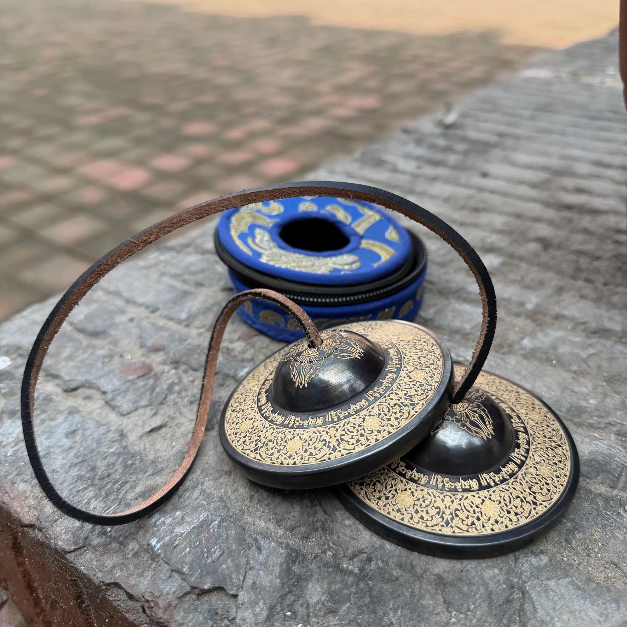 A pair of bronze tingsha cymbals joined by a leather cord